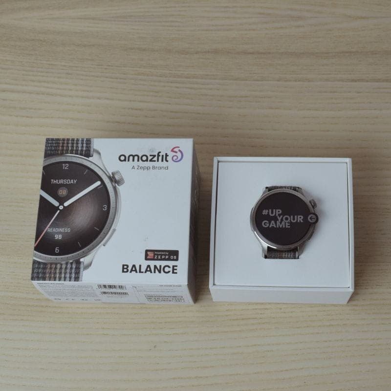 Amazfit Balance cinzento com ecrã AMOLED 1,5 pol no estojo, mostrador redondo prateado, pulseira têxtil cinza e caixa de venda ao lado