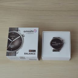 Amazfit Balance cinzento com ecrã AMOLED 1,5 pol no estojo, mostrador redondo prateado, pulseira têxtil cinza e caixa de venda ao lado
