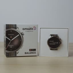 Amazfit Balance cinzento com caixa prateada, mostrador redondo 1,5 polegadas AMOLED e bracelete têxtil listrada; embalagem ao lado do relógio exibido