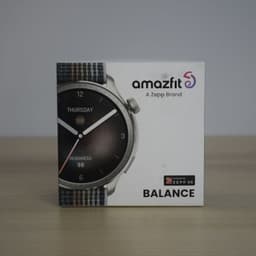 Caixa do Amazfit Balance cinzento com mostrador redondo 1,5 AMOLED, moldura metálica escovada e bracelete têxtil multicolor sobre fundo neutro