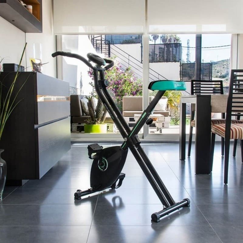 Bicicleta de exercício dobrável X-Bike preta com detalhes verdes, estrutura em X, guidão ergonômico, selim acolchoado e pedais com correias, ideal para uso