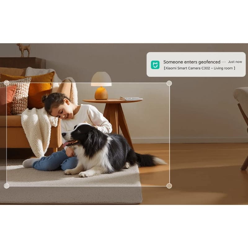 Caméra Xiaomi Smart Camera C302 3MP 2K WiFi 6 posée sur table, s’allume près d’un salon cosy; notifications d’entrée géolocalisée affichées à