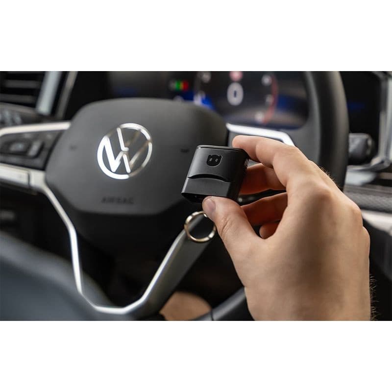 Scanner de diagnostic OBDeleven 3 Pro Pack: petit dongle OBD noir, design compact avec LED, tenu à la main devant un volant de voiture moderne.