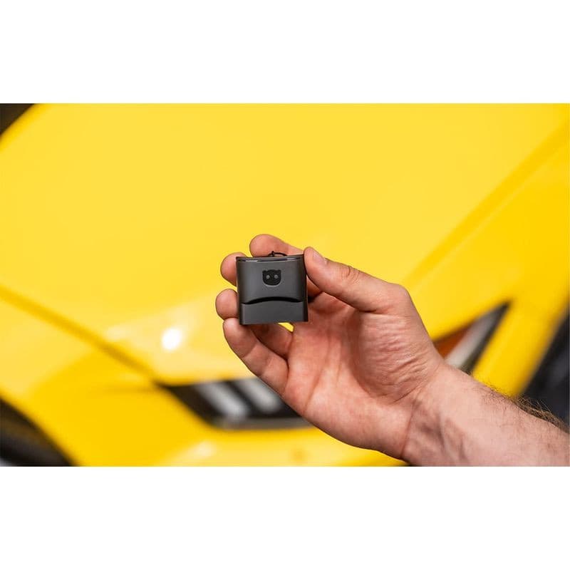 Petit module OBD noir tenu en main devant une voiture jaune; boîtier compact avec voyant et logo, conçu pour le Scanner de diagnostic OBDeleven 3 Ultimate