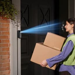 Teclado inteligente com reconhecimento facial projetando feixe azul na porta; mulher aproxima-se com caixas SwitchBot, destacando acesso hands-free e seguro