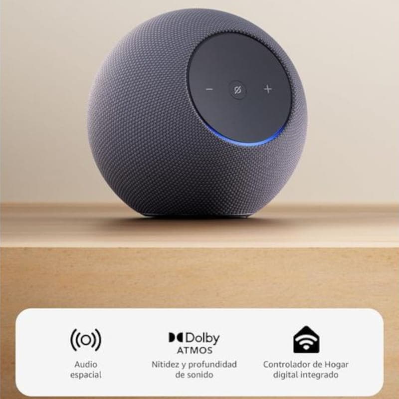 Amazon Echo Studio Grafito esférico con tela gris, panel superior táctil con botones y luz LED azul; base plana. Iconos indican audio espacial y Dolby Atmos