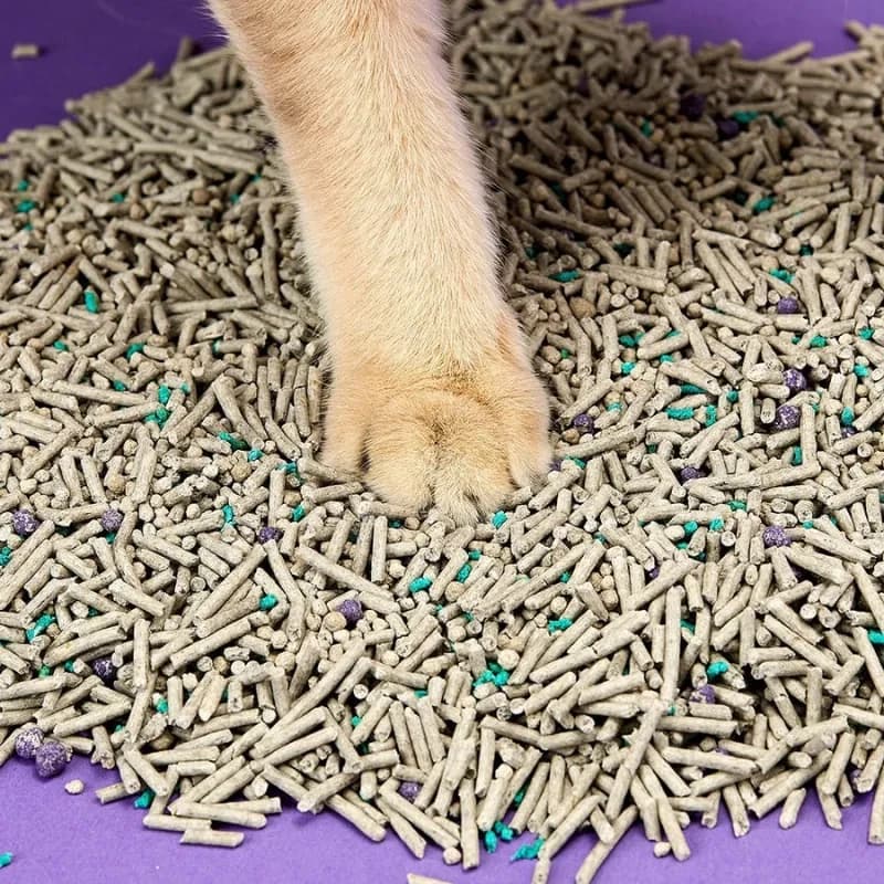 Arena para gatos en pellets beige con partículas verdes y moradas, textura mixta y gránulos uniformes que no se pegan a la pata, ideal para control de olores