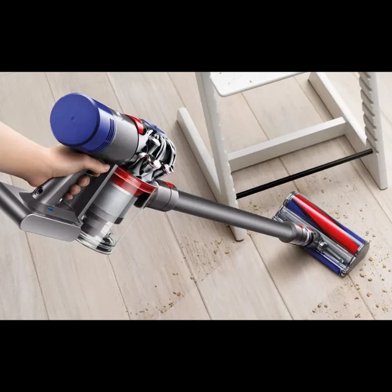 Dyson V8 Cyclone em ação: aspirador sem fios com cabeça motorizada rolo macio, limpa migalhas no chão de madeira; corpo cinza com detalhes vermelhos e azuis