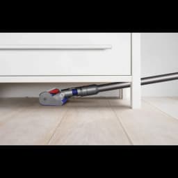 Cepillo motorizado de la Dyson V8 Cyclone limpiando bajo un mueble, diseño bajo perfil con rodillo suave y tubo delgado para acceder a espacios estrechos