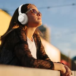 JBL Tune 780NC Beige sur une femme au soleil, arceau rembourré, coussinets circum-auriculaires, design pliable, logo JBL visible, style moderne