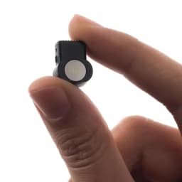 Module caméra XREAL Eye noir avec lentille circulaire blanche, tenu entre les doigts pour montrer sa petite taille et son design minimaliste.