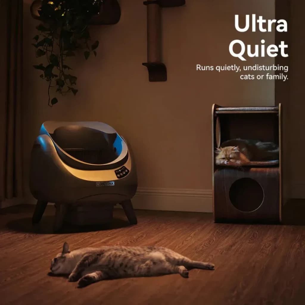 Arenero autolimpiable gris con tapa abierta y panel digital, diseño curvo, silencioso, ideal para gatos; luz tenue azul y acabado moderno en interior hogar