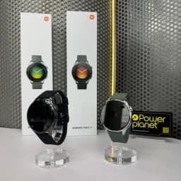 Xiaomi Watch 5 Verde Enebro com caixa prateada, mostrador circular, pulseira verde oliva e display sem conteúdo; ao lado, versão preta e caixas ao fundo