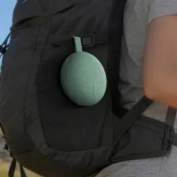 Enceinte portable ronde vert menthe accrochée à un sac à dos noir, tissu maillé, sangle de transport, compacte et légère pour usage extérieur