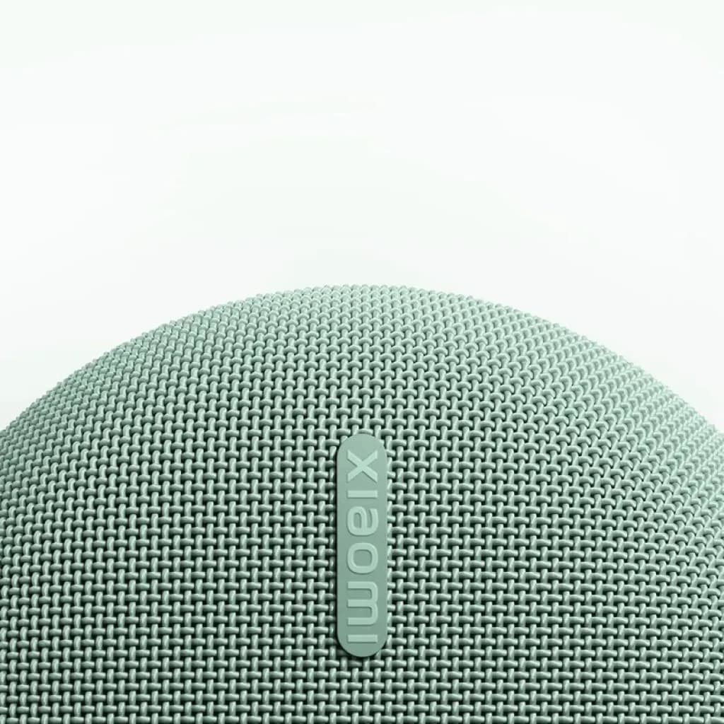Grille textile arrondie vert menthe avec logo Xiaomi en relief, texture maillée fine et bords courbés d’une enceinte portable compacte et élégante
