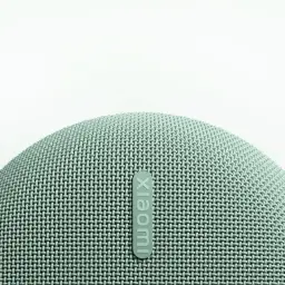 Grille textile arrondie vert menthe avec logo Xiaomi en relief, texture maillée fine et bords courbés d’une enceinte portable compacte et élégante