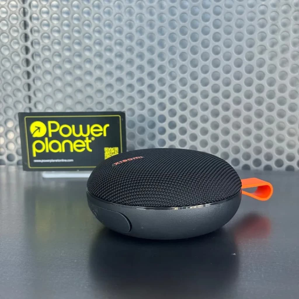 Enceinte portable Xiaomi noire compacte, grille textile noire, base grise mate, lanière orange, bouton latéral discret; design rond moderne et robuste IP66.