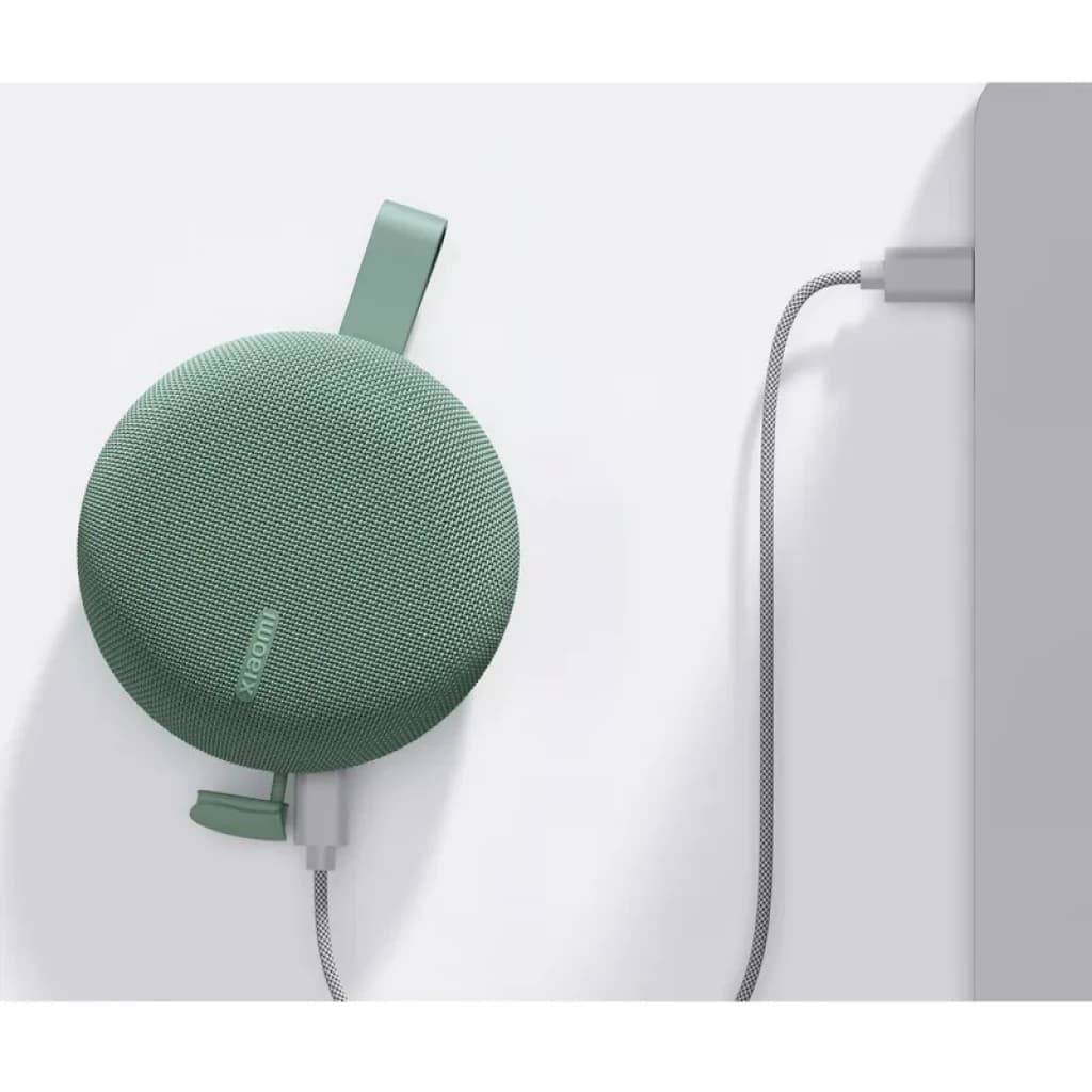Enceinte portable verte compacte avec sangle, grille textile arrondie, logo Xiaomi discret, câble tressé branché sur port latéral, design minimal IP66