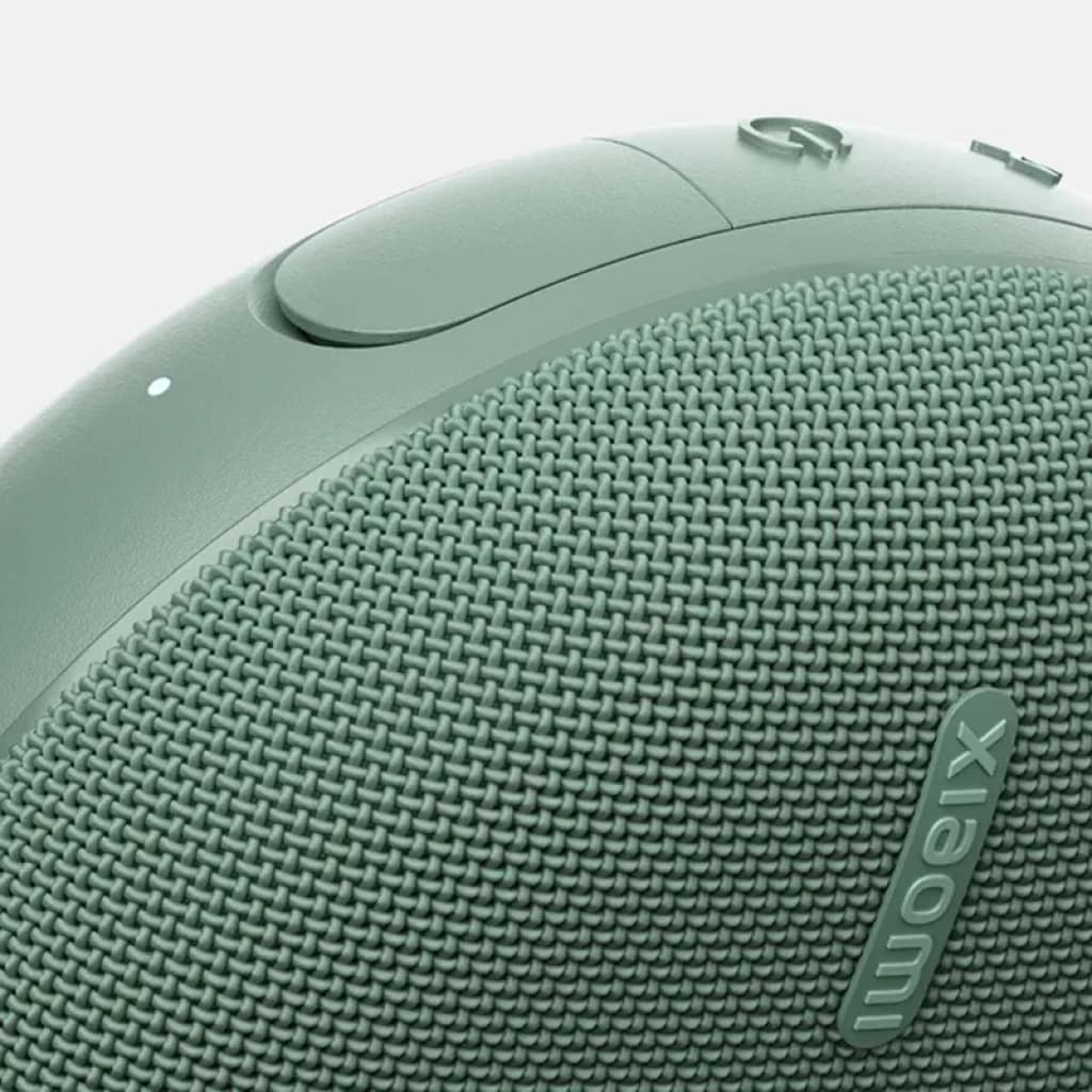 Enceinte portable verte avec tissu maillé, logo Xiaomi en relief, bouton circulaire et LED discrète, bords arrondis au fini mat, design compact et robuste