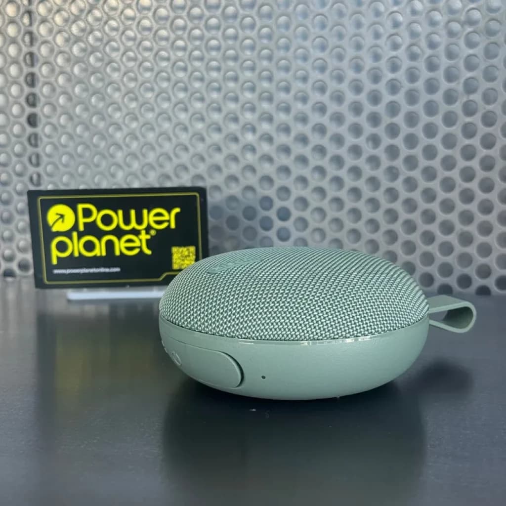Enceinte portable vert sauge compacte 5W avec grille métallique arrondie, bouton latéral, LED et sangle intégrée, design IP66 moderne sur surface sombre