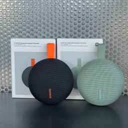 Enceinte portable Xiaomi vert ronde avec tissu maillé, logo vertical, sangle caoutchouc latérale, boîtes arrière montrant versions vert et noire