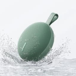Enceinte portable verte ronde avec sangle, grille fine et logo Xiaomi, résistante à l’eau IP66, compacte, éclaboussures visibles, design épuré outdoor