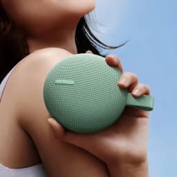 Enceinte portable verte ronde avec grille fine, logo Xiaomi, sangle latérale, format compact tenu en main, design minimal et robuste IP66