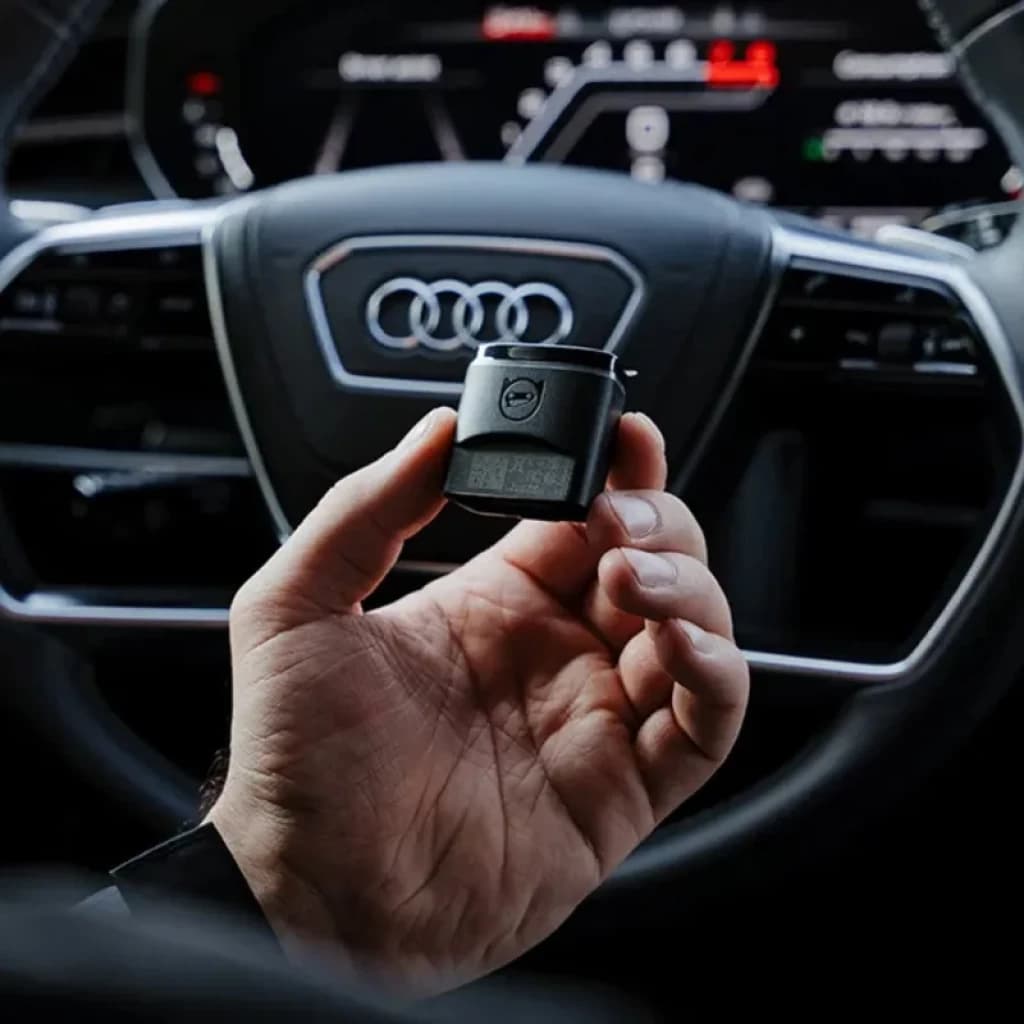 Scanner de diagnostic OBDeleven 2 Pro Pack Programmation VAG Bluetooth BLE tenu en main devant un volant Audi, petit boîtier noir compact avec écran et logo