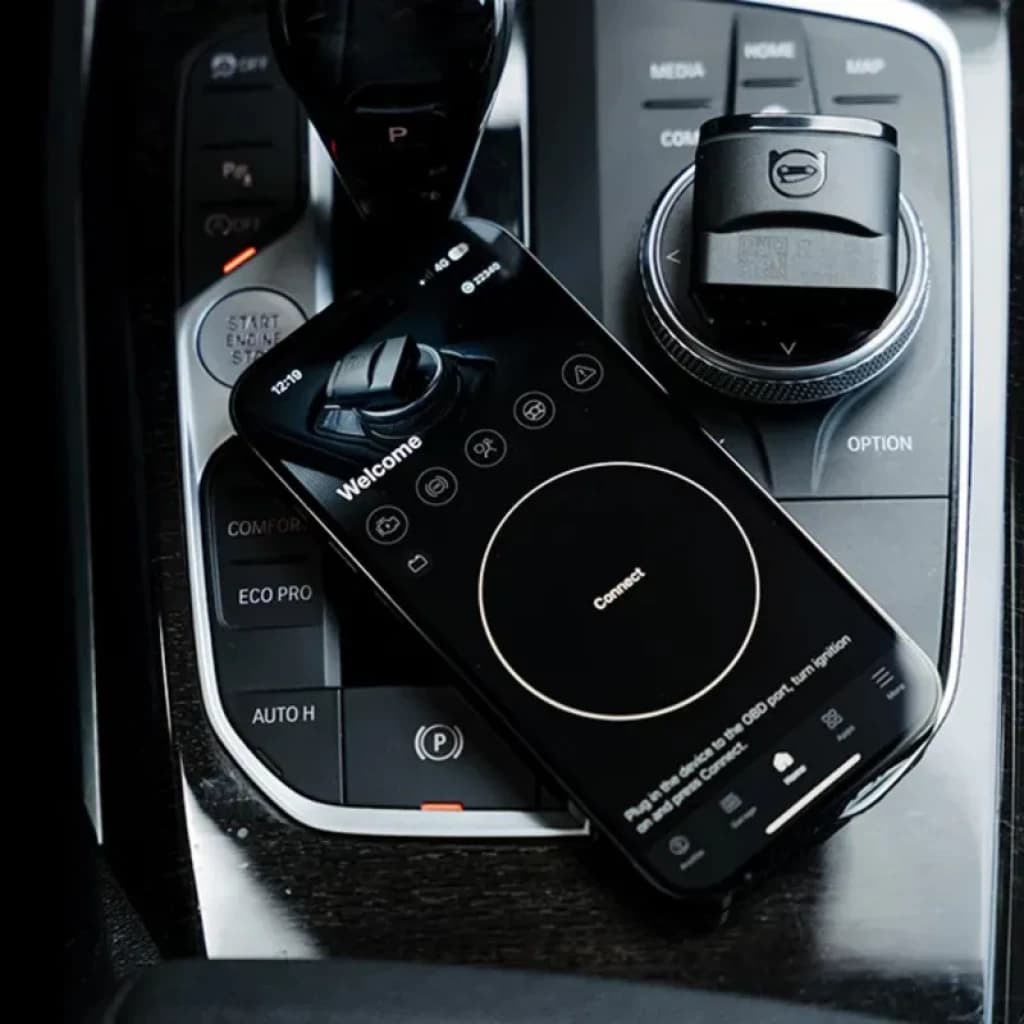 Smartphone affichant lapp OBDeleven posé sur console centrale automobile haut de gamme avec molette et boutons, interface sombre indiquant Connect