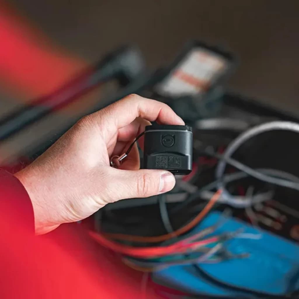Petit adaptateur OBD2 noir OBDeleven 2 Pro Pack avec logo gravé, tenu en main; port compact, cordon de sécurité, câbles et outils auto en arrière-plan
