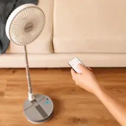 Ventilateur sur pied pliable gris avec télécommande, tête ronde à pales fines, mât télescopique et base stable à boutons bleus, design compact et
