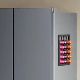 Porte grise avec support mural pour capsules Nespresso, rangées colorées roses, oranges et noires sur un rack magnétique compact