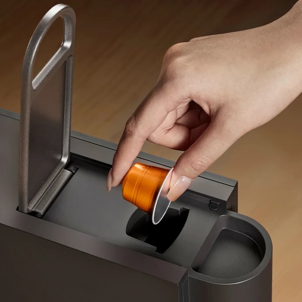 Main insérant une capsule orange dans la Machine à café à capsules Xiaomi Mijia compatible Nespresso, levier métallique et trappe supérieure visibles