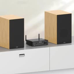 Arylic B50 Amplificador Bluetooth 5.2 negro con antenas duales, panel frontal con perilla y botones, diseño compacto entre dos altavoces de madera clara