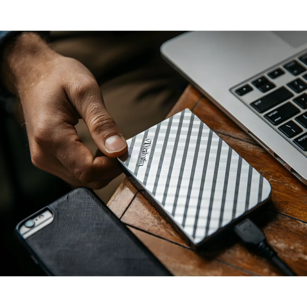Disco Rígido Externo Verbatim Store 'n' Go 2,5 polegadas 1TB USB 3.0 Prata, em uso: mão a ligá-lo a portátil sobre mesa