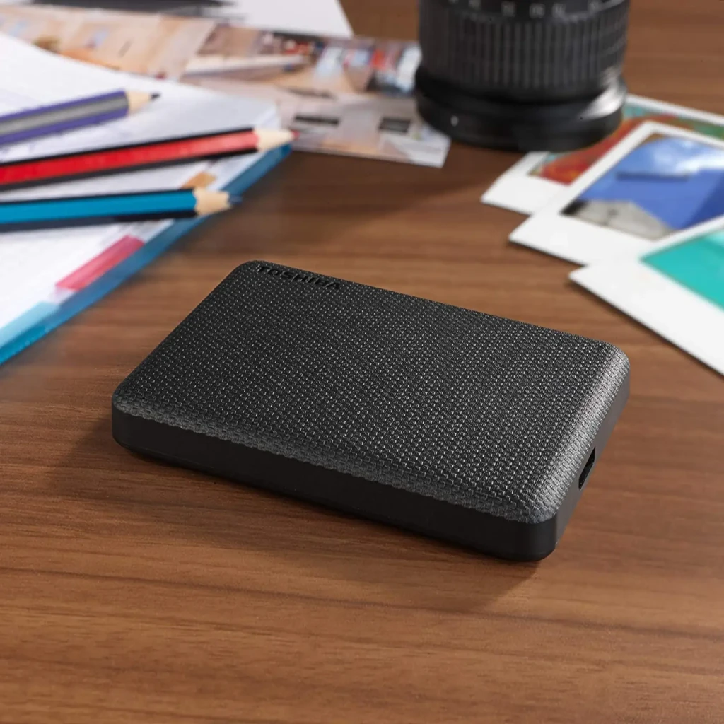 Disque dur externe Toshiba Canvio Advance 2To USB 3.2 Gen 1 Noir, en situation: posé sur bureau en bois avec crayons
