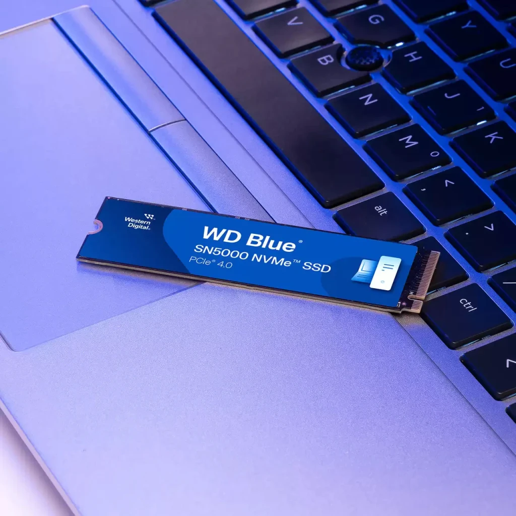 SSD WD Blue SN5000 500GB PCIe 4.0 M.2 2280, en uso: unidad apoyada sobre teclado de portátil con iluminación azul
