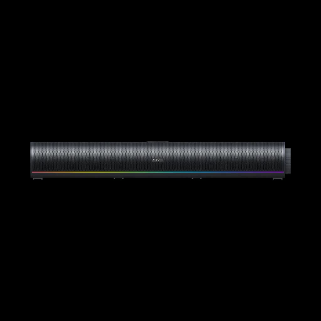 Barra de sonido Xiaomi negra con rejilla metálica frontal, logo central y tira LED RGB en la base, diseño minimalista para escritorio