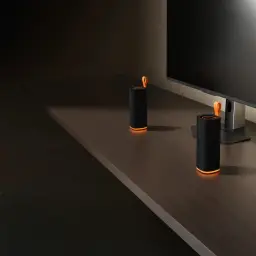 Altavoz Bluetooth Xiaomi Sound Play negro cilíndrico con malla textil, base y asa naranja, luz LED inferior, diseño compacto junto a monitor en escritorio