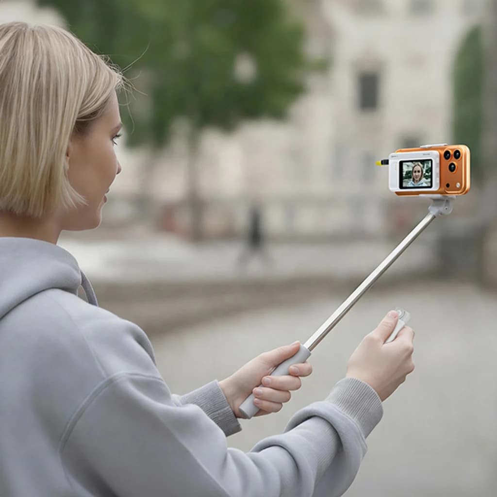 Monitor selfie 7RYMS Qshot V2 4K/60fps MagSafe + USB-C en uso con palo extensible, pantalla frontal mostrando retrato, acabado naranja con botones laterales