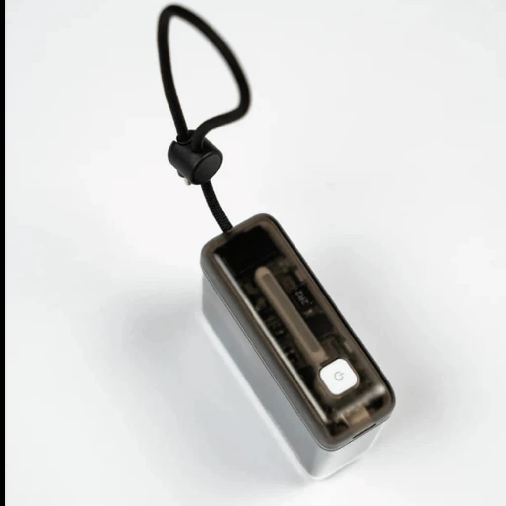 Batterie externe noire compacte avec coque fumée, bouton d’alimentation blanc, câble USB-C intégré visible et dragonne réglable pour transport sécurisé