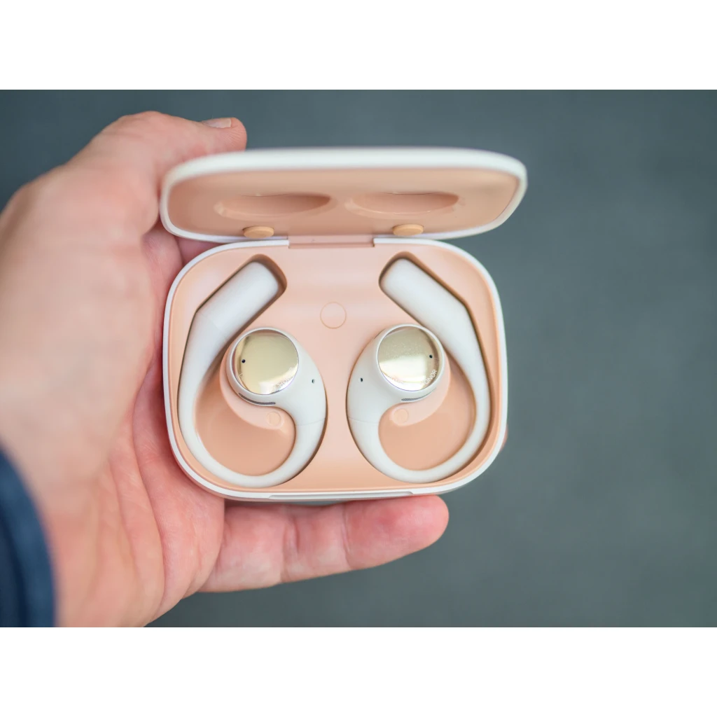 Boîtier beige avec écouteurs open ear à crochet, embouts arrondis, LED frontale et ports de charge internes, design léger et ergonomique Bluetooth 5.2 - Ítem7