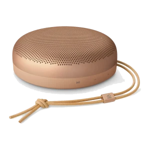 Bang & Olufsen Beosound A1 3rd Gen Honey Tone, vue en angle: forme circulaire, grille perforée et lanière en cuir avec logo
