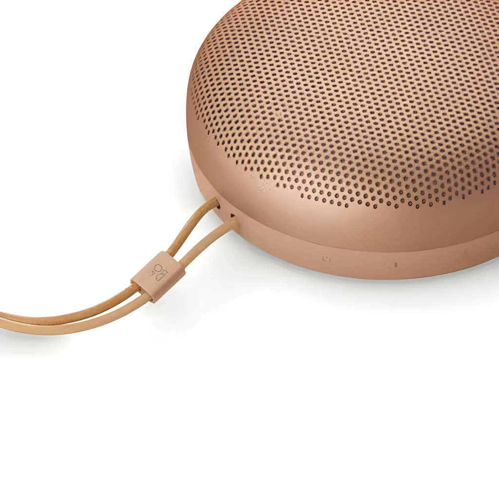 Bang & Olufsen Beosound A1 3rd Gen Honey Tone, vue en angle: forme circulaire, grille perforée et lanière en cuir avec logo - Ítem3