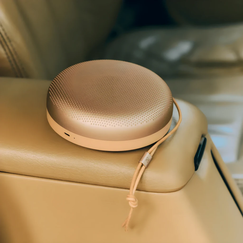 Bang & Olufsen Beosound A1 3rd Gen Honey Tone, vue en angle: forme circulaire, grille perforée et lanière en cuir avec logo - Ítem4
