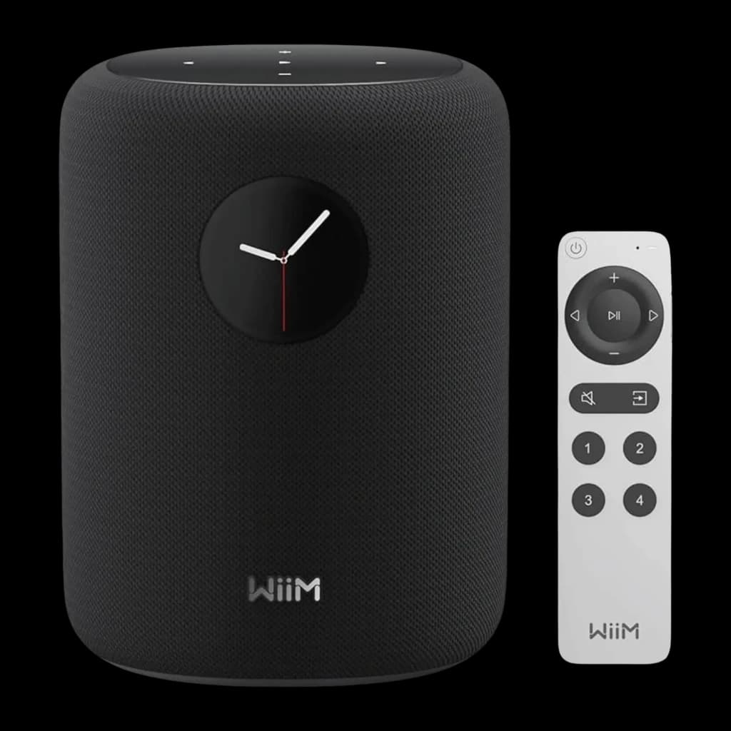 Wiim Sound negro, vista frontal: altavoz cilíndrico con pantalla de reloj analógico y mando a distancia blanco incluido
