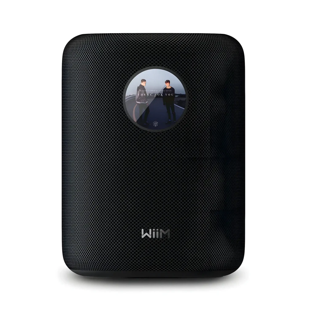 Wiim Sound noir, vue de face: enceinte cylindrique avec affichage horloge analogique et télécommande blanche incluse - Ítem3