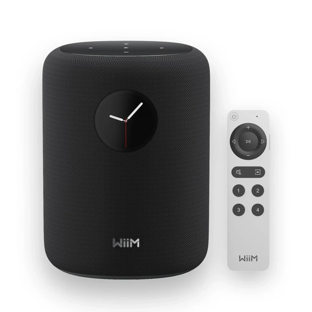 Wiim Sound noir, vue de face: enceinte cylindrique avec affichage horloge analogique et télécommande blanche incluse - Ítem4