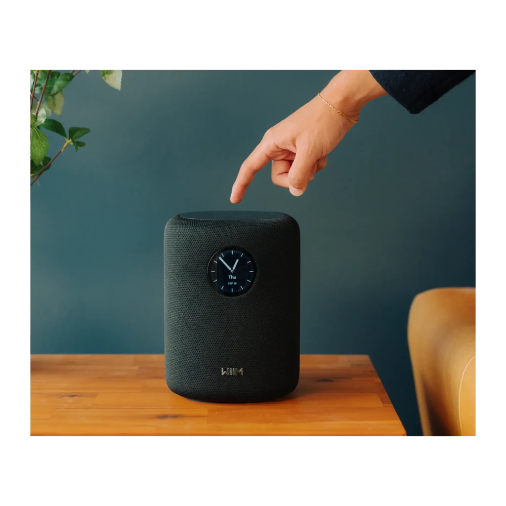 Wiim Sound noir, vue de face: enceinte cylindrique avec affichage horloge analogique et télécommande blanche incluse - Ítem10