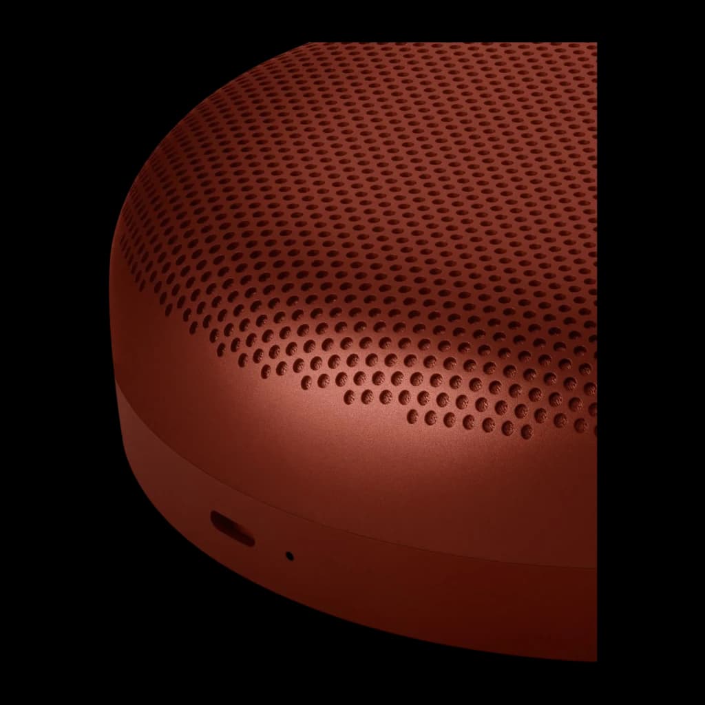 Bang & Olufsen BeoSound A1 3rd Gen rojo, detalle lateral: rejilla perforada y botón en la base sobre fondo oscuro